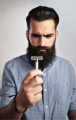 Man with a beard examining a razor closely.
